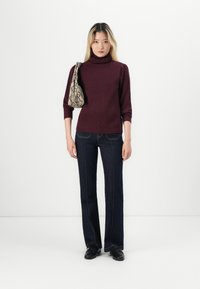 Bourgogne-randig polokrage tröja, utsvängda mörkblå jeans, väska med ormskinnsmönster och svarta skor, stående mot en enkel vit bakgrund.