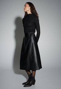 Pull à col roulé noir côtelé associé à une jupe midi en cuir noir. La jupe est dotée d'une taille élastique et d'une texture lisse. Des bottines noires complètent la tenue.