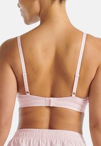 Jasnoróżowy biustonosz z regulowanymi ramiączkami, zapięciem na haftkę oraz cienkiego materiału. Gładka faktura, prosta forma i minimalne detale.