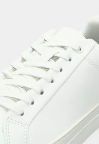 Λευκά sneakers με λείο συνθετικό υλικό, στρογγυλή μύτη, επίπεδα κορδόνια και ελάχιστες λεπτομέρειες ραψίματος.