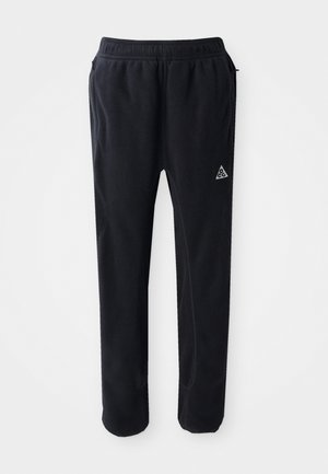 Schwarze Sporthosen aus einem weichen, strukturierten Material, mit einem elastischen Bund, seitlichen Taschen und einem dreieckigen Logo-Akzent am Oberschenkel.