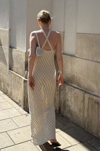Pleteni maksi oblek v bež barvi s chevron vzorcem in križnimi naramnicami, združena s krožno belo torbico z izrezljanim dizajnom.