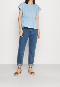Top peplum azzurro chiaro realizzato in tessuto morbido con maniche corte, abbinato a jeans scuri arrotolati e sandali marroni con fasce.