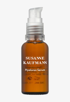 Brązowa szklana butelka z białym dozownikiem pompkowym, oznaczona "SUSANNE KAUFMANN Hyaluron Serum." Minimalistyczny design, nieprzezroczysta obudowa.