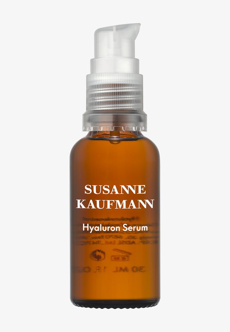 Bouteille en verre brun avec un distributeur à pompe blanc, étiquetée "SUSANNE KAUFMANN Sérum Hyaluron." Design minimaliste, corps opaque.