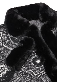 Cappotto a fantasia bianco e nero con colletto e polsini in morbido pelo sintetico nero; presenta un dettaglio con zip sul lato.