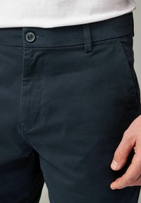 Pantalones de algodón de un oscuro color navy con una textura suave, que presentan un cierre frontal con botón, presillas para cinturón y bolsillos laterales.