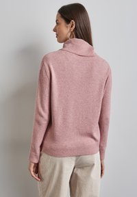 Rosa, tjockstickad polotröja med ribbade ärmmuddar och nederkant, med en avslappnad passform. Bärs tillsammans med ljusbeige kordfläskbyxor.
