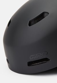 Matná čierna prilba s ventilačnými otvormi a textúrovaným interiérom. Na boku má detail loga, navrhnutá pre bezpečnosť a pohodlie.