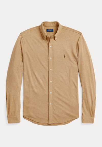 Camisa de manga longa, de cor bege, feita de um tecido macio. Apresenta um colarinho clássico, fecho por botões e um pequeno logotipo no peito.
