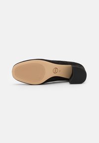 Zapato de tacón de ante negro con puntera redonda y suela de goma beige suave, que presenta estrías horizontales para mayor tracción y un pequeño tacón.