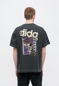 Fekete, túlságosan nagy póló, hátulján nagy "adidas" logó krémszínben, valamint egy színes grafikával, amely egy biciklit és absztrakt mintákat ábrázol.