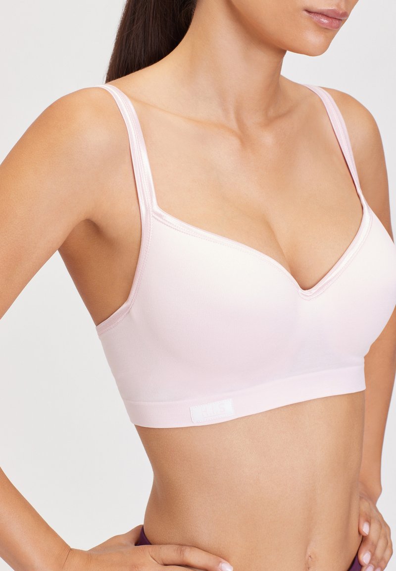 Soutien-gorge seamless rose avec un décolleté en V, bretelles réglables et une large bande inférieure douce ornée d'une petite étiquette logo. Texture lisse.