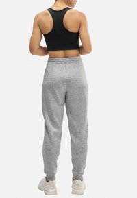 Sostén deportivo negro de tirantes cruzados combinado con pantalones de chándal grises, que cuentan con una cintura ajustable y puños acampanados. Zapatillas completas el conjunto.