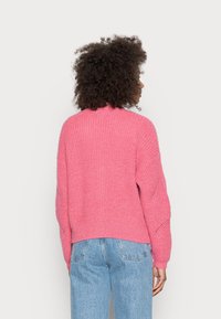 Rosa stickad tröja med avslappnad passform, med ribbad textur och sänka axlar, kombinerad med blå denimjeans.