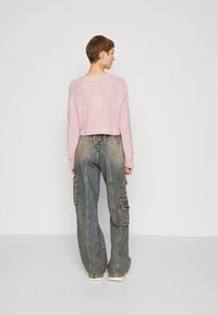 Avskuren rosa stickad tröja med mönster i struktur, ihop med lösa, urblekta blå jeans med cargofickor och en avslappnad passform.