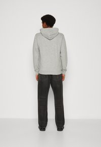 Gray sweatshirt with a hood, featuring ribbed cuffs and hem. Worn with black faded jeans. Background is plain and white.