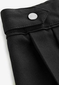 Tissu plissé noir avec une texture lisse. Présente un bouton en métal gravé "Clarks". Comprend une taille structurée.