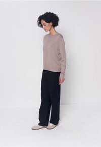 Pull en tricot marron clair associé à un pantalon noir à jambes larges et des baskets beiges. Le modèle présente une coupe décontractée et un col rond.