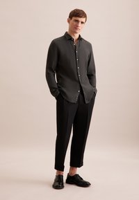 Camicia grigia con bottoni realizzata in tessuto testurizzato, abbinata a pantaloni neri a gamba stretta e scarpe nere. La camicia presenta un colletto classico e un leggero luccichio.
