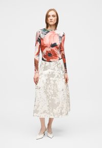 Μπλούζα με μακριά μανίκια και λουλουδάτο μοτίβο σε αποχρώσεις του κόκκινου και ροζ, συνδυασμένη με υφασμάτινη λευκή μίντι φούστα με λουλουδάτο σχέδιο. Λευκά ψηλοτάκουνα.