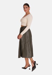 Top corto de manga larga crema con textura acanalada y falda midi plisada verde oscuro, combinados con tacones slingback negros con detalles metálicos.