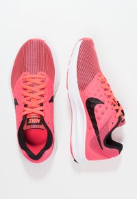 Baskets de course Nike en mailles roses vives, avec des accents noirs, texture hexagonale et semelle blanche. Les lacets sont de couleur rose assortie.