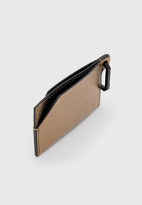 Tarjetero metálico dorado delgado con bordes negros y un clip de mosquetón de plástico negro sobre un fondo blanco.