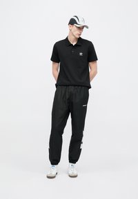 Mustast polost valge logoga, koos mustade, elastse vöökohaga tuulekindlate pükstega, millel on hallid detailid, ning valgete kingadega halli kujundusega.