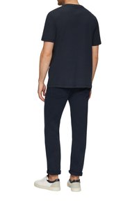 Marineblauw T-shirt met korte mouwen, losse pasvorm, van katoen, gecombineerd met donker marineblauwe slim-fit broek en witte schoenen met marineblauwe accenten.