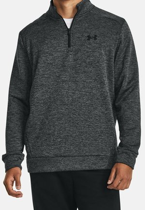 Mann trägt dunkelgrauen Viertel-Reißverschluss-Pullover mit subtiler Melierung und schwarzem Under Armour-Logo auf der Brust.