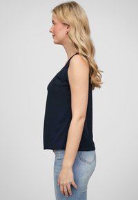 Top sans manches bleu marine à coupe décontractée avec de légentes fentes sur les côtés, associé à un jean ajusté bleu clair. Tissu lisse avec un minimum de détails.