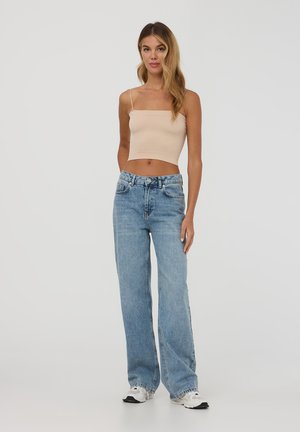 Top cropped a coste beige, jeans a gamba larga blu chiaro e sneakers bianche. L'outfit presenta un design casual con dettagli minimi.