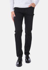 Pantaloni in cotone neri con vestibilità slim, abbinati a scarpe nere lucide. Il maglione è grigio chiaro con un motivo a maglia testurizzata.