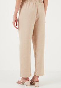 Beige linnen broek met een losse pasvorm, elastische tailleband en rechte snit. Gladde textuur en minimale details, gecombineerd met lichte hakken.
