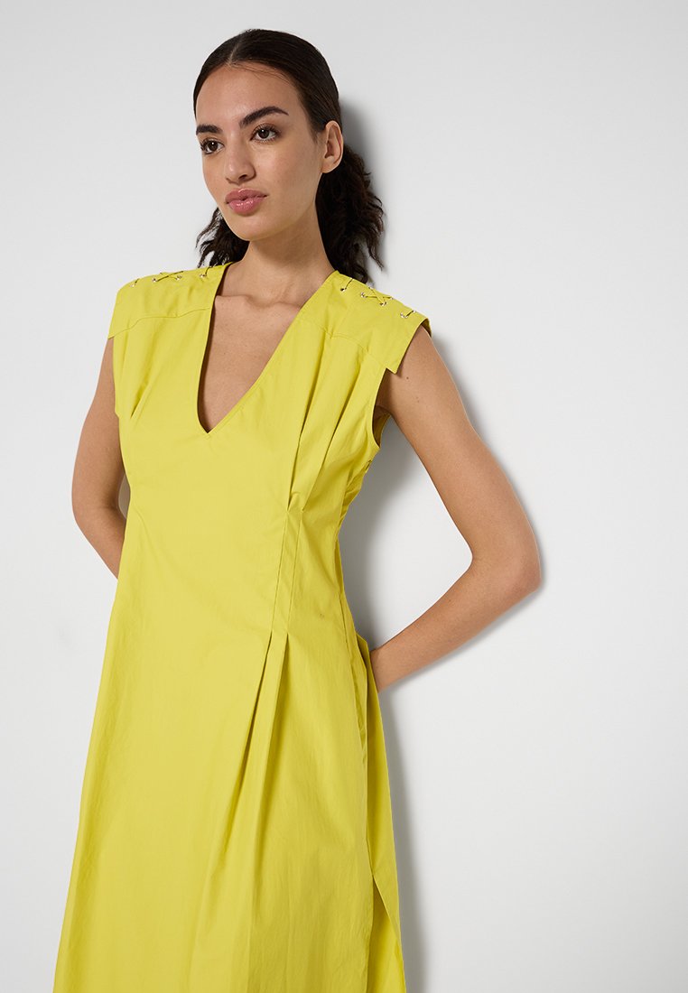 Gul klänning med V-ringning, korta ärmar och sidofållar. Har dekorativ sömnad vid axelsömmarna. Slätt, lätt tyg.