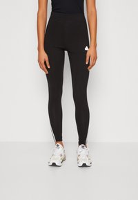 Leggings pretas com uma cintura alta, riscas brancas nas laterais e um pequeno logótipo branco na coxa; feitas de um tecido elástico para maior conforto.