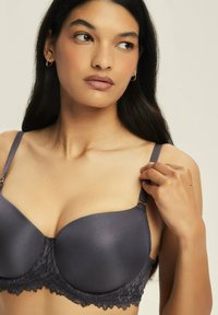 Szary biustonosz z podkładem, z koronkowymi detalami na obwodzie, regulowanymi ramiączkami i gładkim wykończeniem. Posiada zapięcie na hak i oczko dla lepszego wsparcia.