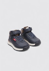 Zapatos para niños en azul marino con parte superior sintética lisa, puntera redonda, cierre de cordones y tira de Velcro, y entresuela blanca con detalles en gris.