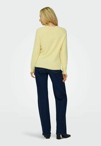 Pull en maille jaune clair avec un col rond, associé à un jean large bleu foncé et des chaussures à talons noires. Design simple, sans motifs.