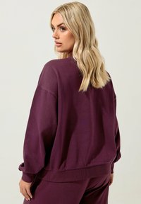 Bordo ylityöskentelijähuppari, jossa on pyöreä pääntie, ribbaustaskut ja helma. Pehmeä kangas, jossa on sileä pinta ja vähäisiä ompelutietoja.