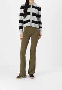 Harmaa ja musta raitapaita, jossa on pyöreä kaulus, napit edessä ja aaltoileva helma, yhdistettynä oliivinvihreisiin leveälahkeisiin housuihin ja mustiin lenkkareihin.