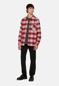 Rood en wit geruite flanellen shirt met een borstzak, gelaagd over een donkergrijs t-shirt, gecombineerd met zwarte broek en zwarte schoenen.