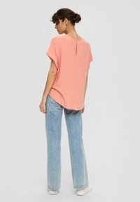 Helles rosa T-Shirt mit kurzem Ärmel und einem Schlüssellochdetail im Rücken, kombiniert mit hoch taillierten hellblauen Jeans und weißen Sneakers. Weicher Stoff.