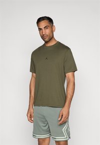 Λάδι πράσινο κοντομάνικο μπλουζάκι με στρογγυλή λαιμόκοψη και μαύρο λογότυπο. Συνδυασμένο με ανοιχτό γκρι σορτσάκι με τρυπητή υφή και γραφικά στοιχεία.