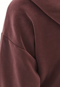 Bordowy sweatshirt o gładkiej fakturze, z zaokrąglonym szwem na ramieniu i subtelnym detalem kieszeni. Gruby materiał o luźnym kroju.