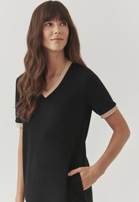 Black dress with a V-neck and short sleeves, featuring beige accents on the neckline and cuffs. Includes a side pocket. Soft fabric texture.