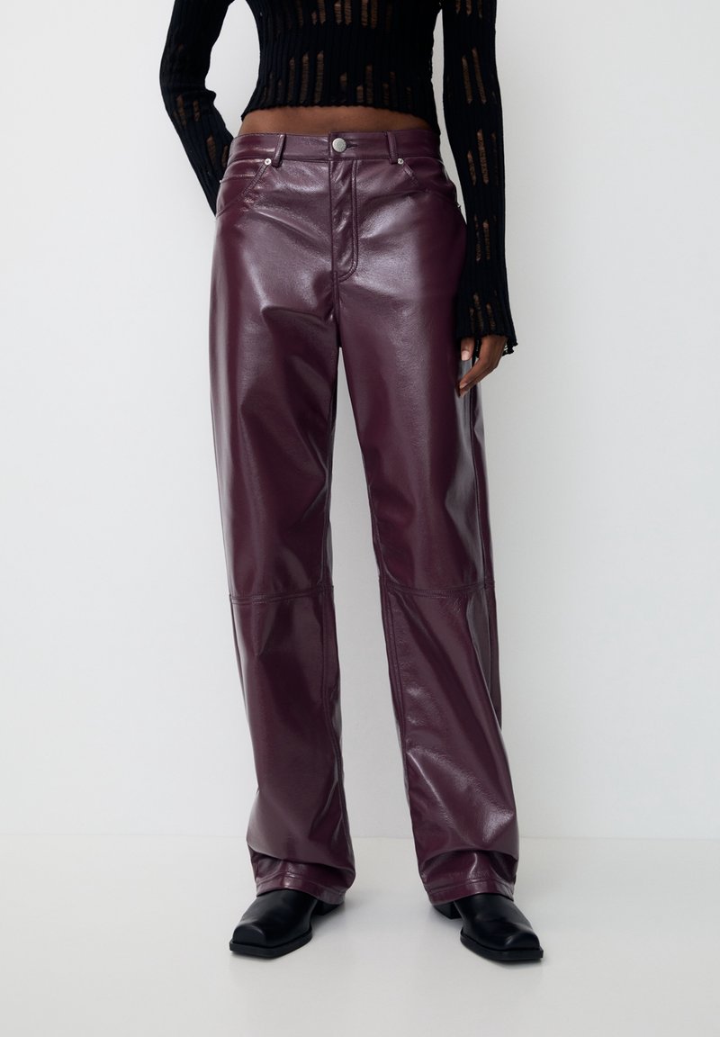 Pantalon en cuir violet foncé brillant porté avec des bottes noires à bout carré et un haut noir texturé à manches longues partiellement visible.