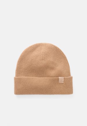 Brown ribbed beanie hat made of soft fabric, featuring a rolled cuff and a small branded tag on the side.