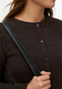 Brūns adīts kardigans ar apaļu kakla izgriezumu, trīs pogām un ribotām aprocēm; valkāts ar melnu ādas siksnu.